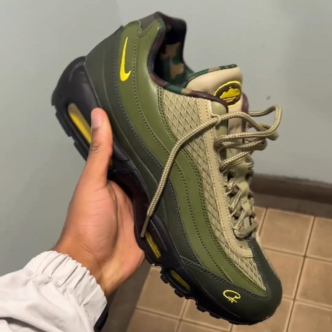 Hand holding a green sneaker with a yellow logo against a plain background