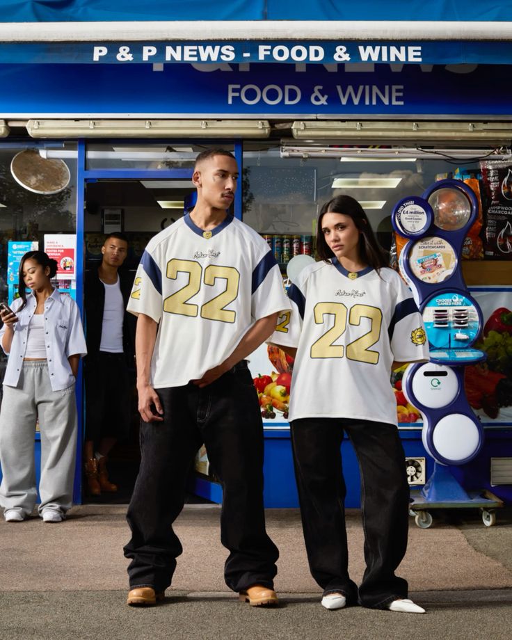 Two people wearing matching jerseys with the number 22 in front of a store named 'P & P News - Food & Wine'.