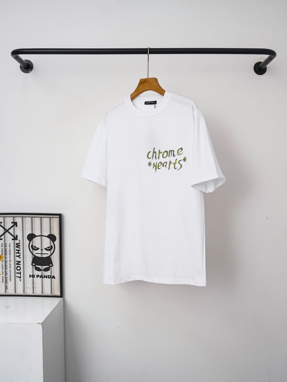 White t-shirt with text hanging on a rack against a white wall.
