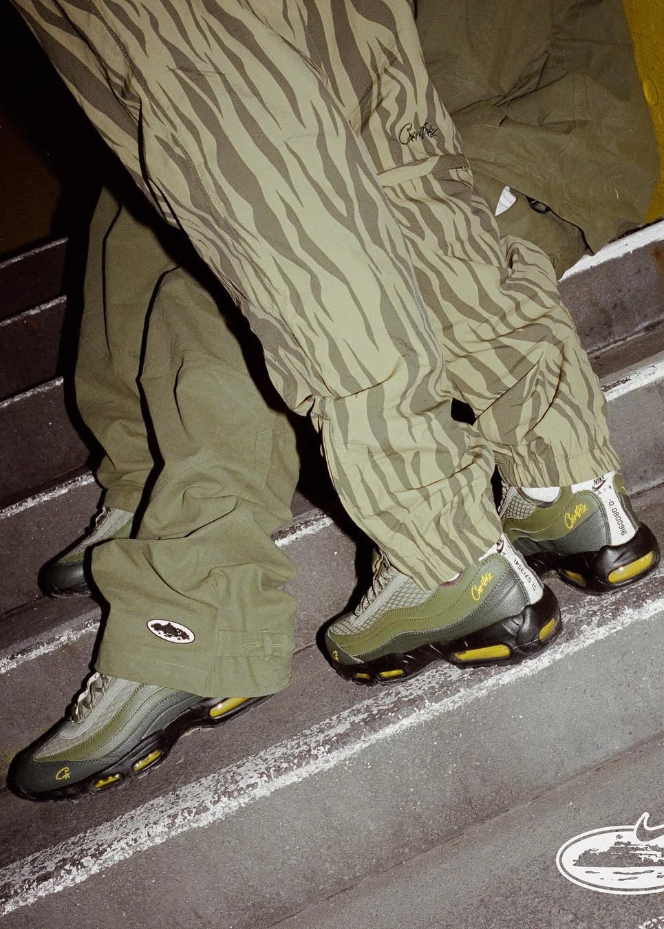 Person wearing green camouflage pants and shoes walking up stairs with a Nike logo visible.