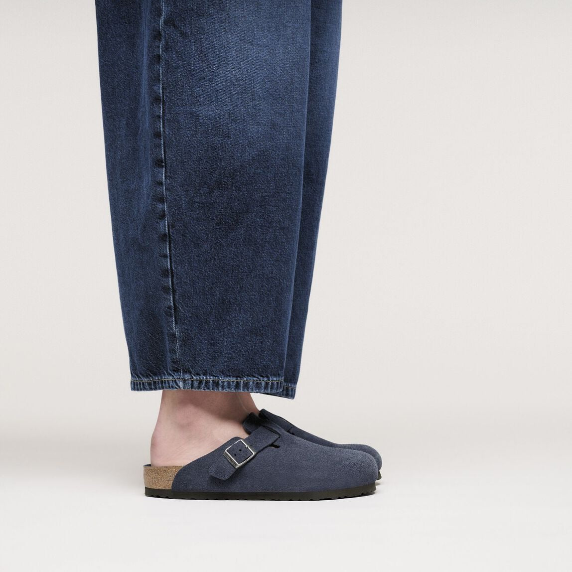 Person wearing blue denim pants and navy clogs on a light background