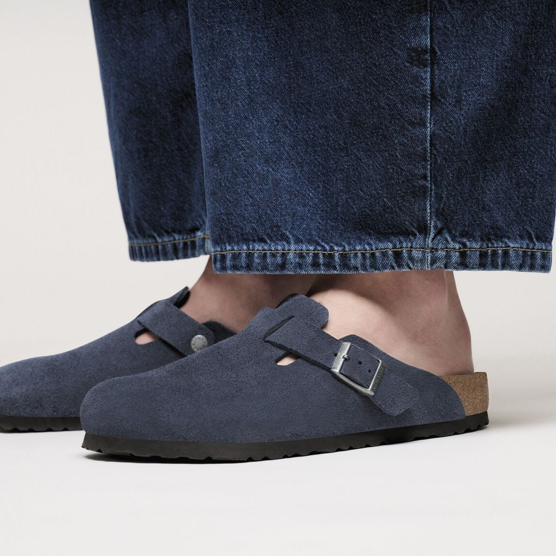Navy blue suede shoes with brown soles worn with blue jeans on a light background