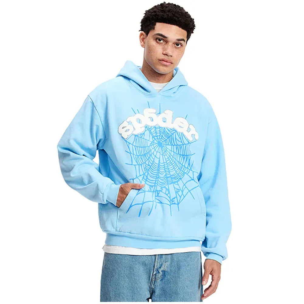 A young man modeling a light blue pullover hoodie with a white 'spideon' text graphic and a blue spiderweb design on the front, paired with blue jeans against a plain white background.