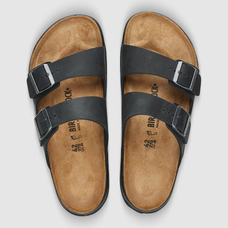 A pair of Birkenstock Arizona double-strap slide sandals shown from a top-down view. The sandals feature black leather straps with silver metal buckles and a natural tan cork footbed.