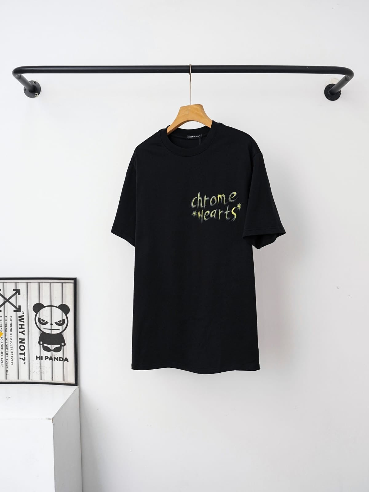 Black t-shirt with text on a hanger against a white wall